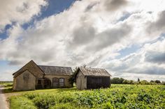 an old farm house sitting in the middle of a green field under a cloudy sky