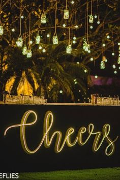 a sign that says cheers with lights hanging from the ceiling and trees in the background