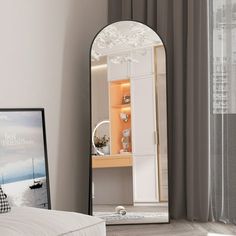 a mirror sitting on top of a white bed next to a window with curtains over it