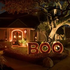 the word boo spelled out in front of a house at night with lights on it