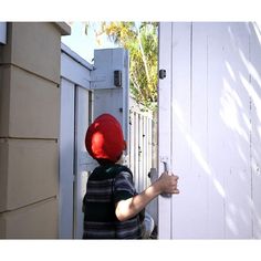 a young boy wearing a red helmet opens the door to his house with one hand