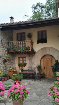 an outdoor patio with potted plants and flowers in front of a house that has stone walls