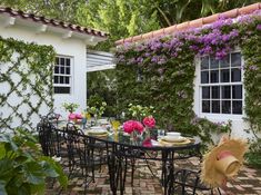 an outdoor dining area with tables and chairs in front of a house covered in purple flowers