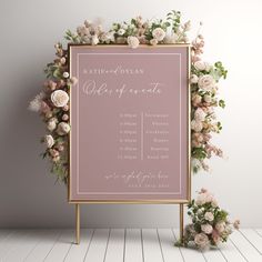 a pink sign with flowers on it next to a white wall and wooden flooring