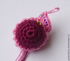 a crocheted pink flower with green and blue dots on the end, sitting on a white surface