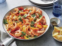 shrimp and bell pepper stir fry in a pan with lemon wedges on the side