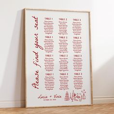 a red and white wedding seating chart on a wooden frame in front of a wall