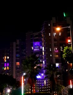 a city street at night with tall buildings lit up in purple and green lights on the side