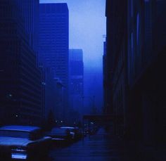 cars parked on the side of a city street with tall buildings in the background at night