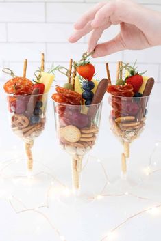 three glasses filled with fruit and crackers on top of a white table next to a hand