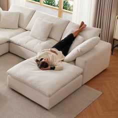 a person laying on top of a white couch in a living room next to a window