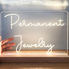 a person's hand is holding up a neon sign that says permanent jewelry on it