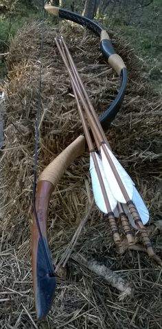 two bows and arrows are laying on the ground next to some hay, with another bow in the foreground