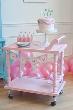 a pink cart with balloons and cake on it