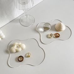 two glass plates with rings on them next to some wine glasses and seashells