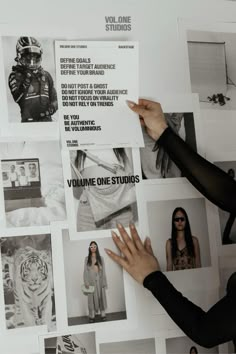 a woman in black shirt pointing at wall with pictures on it