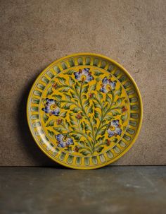 a yellow and blue plate sitting on top of a stone floor next to a wall