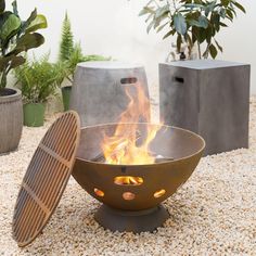 a fire pit sitting on top of a pile of gravel next to potted plants