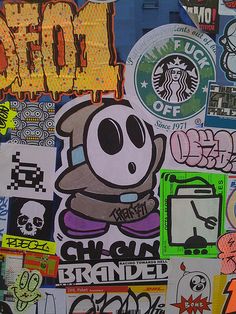 a bunch of stickers are on the side of a wall that is covered in graffiti