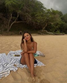 a woman sitting on top of a beach next to a towel