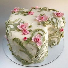 a white cake decorated with pink flowers and leaves on a silver platter in the shape of a heart