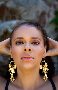 a woman with her hands on her head, wearing gold earrings and black tank top