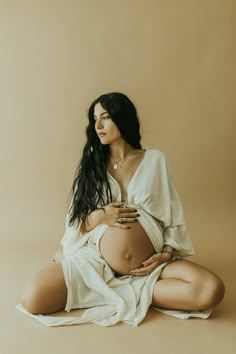 a pregnant woman sitting on the floor with her belly wrapped in a white blanket and holding her hands to her stomach