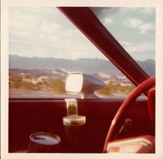 an old photo of a car driving down the road with mountains in the background and clouds in the sky