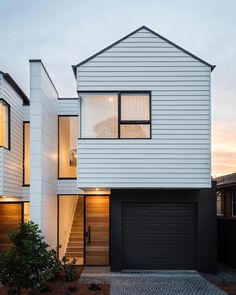 two story house with white siding and black garage doors on the outside, surrounded by brick pavers