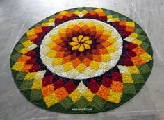 a multicolored circular rug on the floor with an orange, yellow and red flower