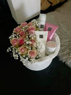 a white basket filled with lots of pink and white flowers next to a candle on top of a rug