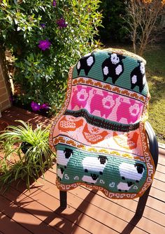 a colorful chair sitting on top of a wooden deck next to a flower pot filled with purple flowers