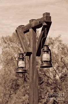 an old fashioned wooden post with two hanging lanterns on it's side and trees in the background