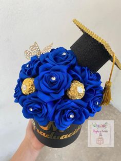 a blue rose bouquet in a black box with gold accents and a graduation cap on top