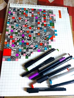 pens and markers are lined up next to a piece of paper that has squares on it