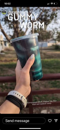 someone holding up a cup with gummy worm on it in front of a fence