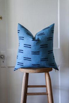 a blue pillow sitting on top of a wooden stool next to a white wall and door