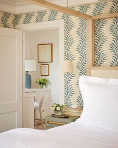 a white bed sitting in a bedroom next to a wallpaper covered with blue and white leaves