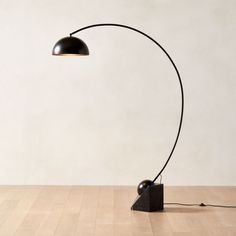 a floor lamp with a black shade on the base and a white wall in the background