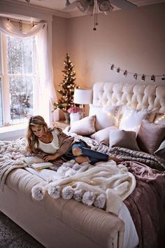 a woman sitting on top of a bed next to a christmas tree in a bedroom