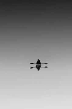 a black and white photo of a person in a boat with oars on the water