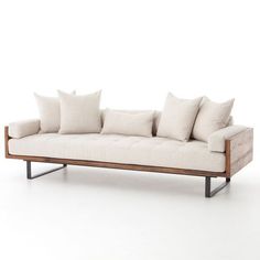 a white couch with four pillows on it's back and two arms, sitting in front of a white wall