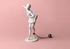 a white figurine is chained to a black ball on a pink background with a chain