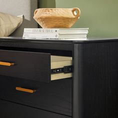 a wooden bowl sitting on top of a black dresser next to books and a pillow