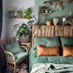 a bed with green sheets and pillows next to a shelf filled with potted plants