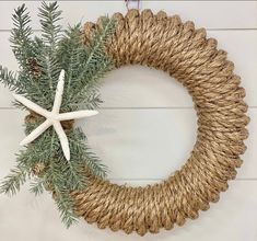 a rope wreath with starfish and evergreen branches hanging on a white wooden wall behind it