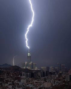 a lightning bolt is seen in the sky over a city at night with skyscrapers lit up