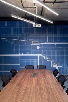 an empty conference room with blueprinted walls and wooden table in the center, surrounded by black chairs