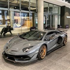 a grey sports car parked in front of a glass building with an elephant statue behind it