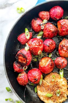 a skillet filled with meat and vegetables on top of a white countertop next to green onions